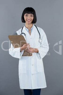 Doctor holding clipboard against grey background