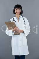 Doctor holding clipboard against grey background