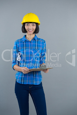 Female architect holding clipboard and blueprint against grey background