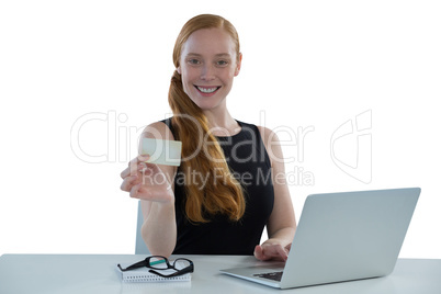 Female executive holding visiting card while using laptop