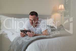Man lying on bed and using digital tablet in bedroom