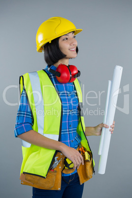 Female architect holding blueprint against grey background