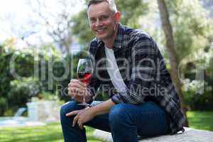 Smiling man having glass of red wine in garden