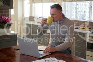 Man using laptop while having cup of coffee in living room