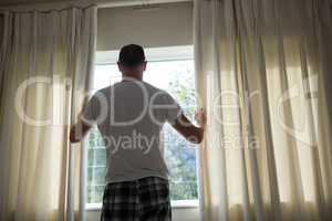 Man opening window curtain in bedroom