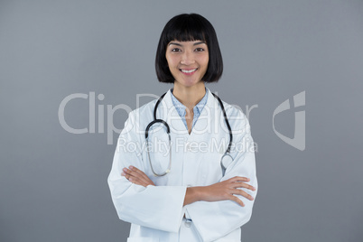 Doctor standing with arms crossed against grey background