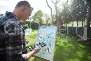 Man painting on canvas in garden