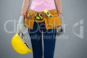 Woman with tool belt and holding hard hat against grey background