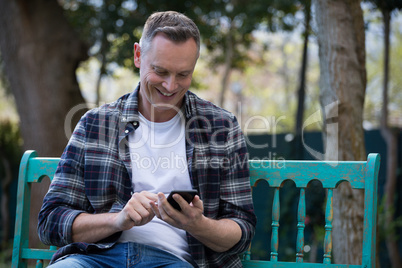 Man using mobile phone on bench in garden