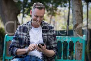 Man using mobile phone on bench in garden