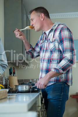 Man tasting food while preparing in kitchen