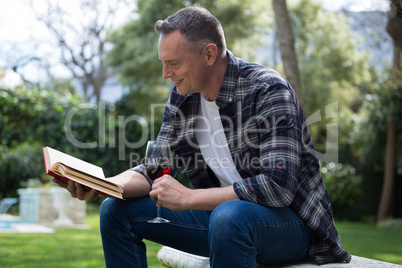 Man reading novel while having glass of red wine