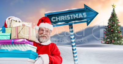 Christmas text and Santa holding gifts with Wooden signpost in Christmas Winter landscape with Chris