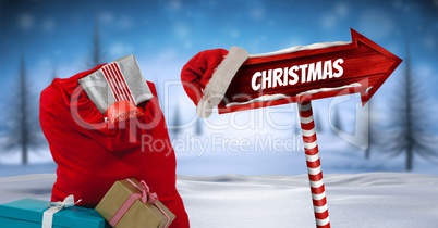 Christmas text and gifts with Wooden signpost in Christmas Winter landscape and Santa hat with Chris