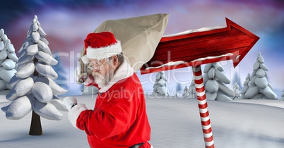 Santa carrying sack and Wooden signpost in Christmas Winter landscape
