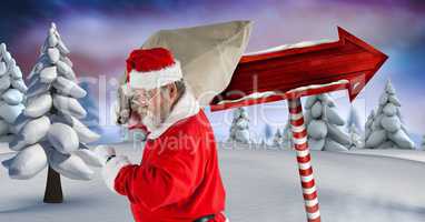Santa carrying sack and Wooden signpost in Christmas Winter landscape