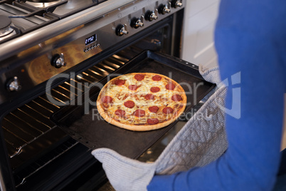 Man putting pizza into oven in kitchen