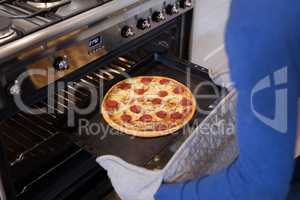 Man putting pizza into oven in kitchen
