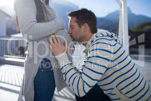 Man kissing belly of pregnant woman in balcony