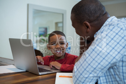 Father and son using laptop in living room