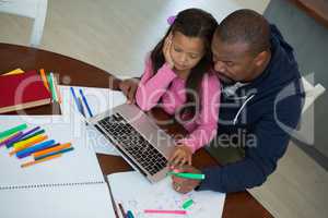 Father and daughter using laptop in kitchen