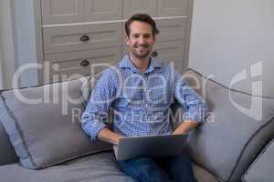 Happy man using laptop while relaxing on sofa