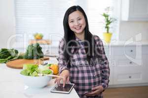 Pregnant woman using digital tablet in kitchen