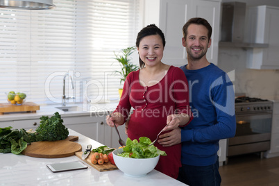 Pregnant couple preparing salad together in the kitchen
