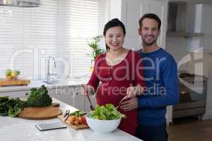Pregnant couple preparing salad together in the kitchen