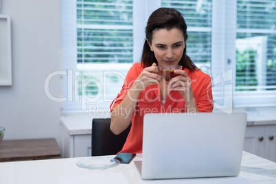 Woman using laptop while having lemon tea in kitchen