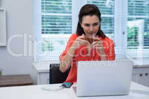 Woman using laptop while having lemon tea in kitchen