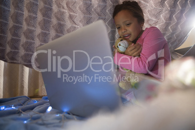 Girl holding teddy bear and looking at laptop