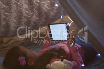 Girl using digital tablet under blanket in bedroom