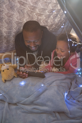 Father and daughter using digital tablet in bedroom