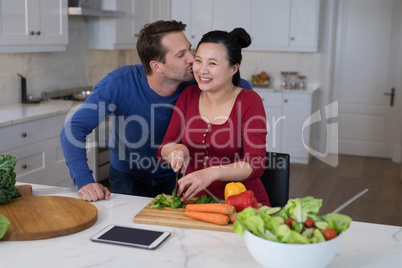Man kissing the woman while chopping vegetables