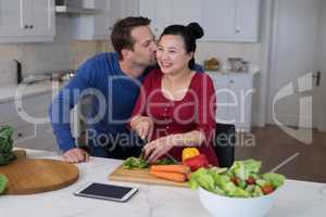 Man kissing the woman while chopping vegetables