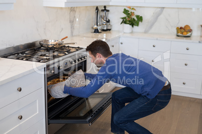 Man putting pizza into oven in kitchen
