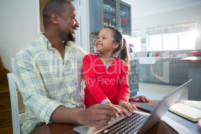 Father and daughter using laptop in kitchen