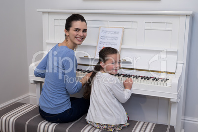 Portrait of mother assisting daughter in playing piano