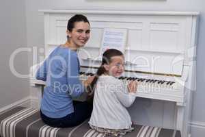 Portrait of mother assisting daughter in playing piano