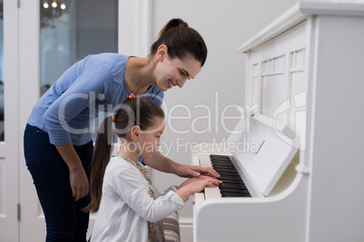 Mother assisting daughter in playing piano