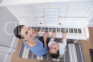 Overhead of mother assisting daughter in playing piano