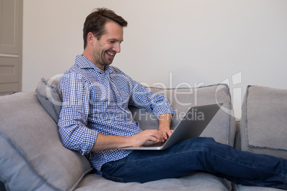 Happy man using laptop while relaxing on sofa