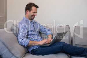 Happy man using laptop while relaxing on sofa