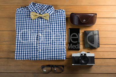 Folded shirt, spectacle, camera, wallet, and mobile phone on wooden plank