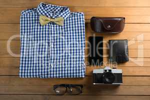 Folded shirt, spectacle, camera, wallet, and mobile phone on wooden plank