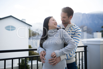 Man and pregnant woman touching her belly in balcony