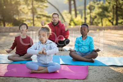 Coach and kids meditating in park