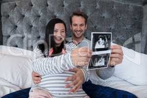 Portrait of man and pregnant woman holding sonography