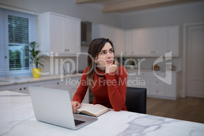Woman sitting with laptop and book at desk